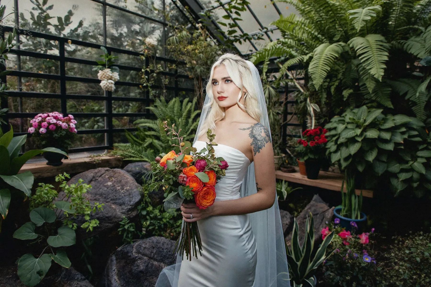 Bride holding an orange bouquet among ferns and flowers in a conservatory