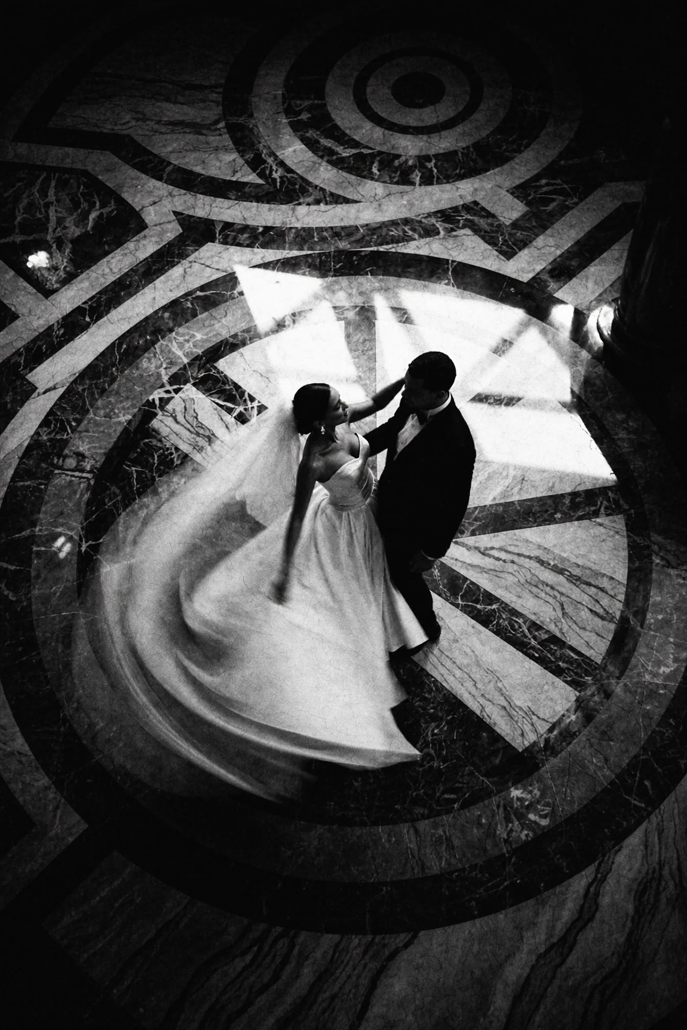 Overhead black and white frame of a couple dancing alone on a spiral marble floor