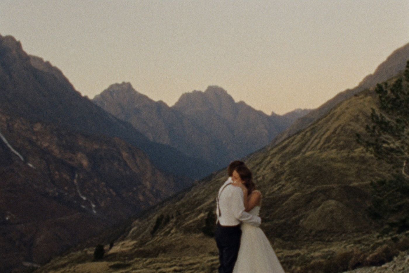 A couple embracing alone at the edge of a vast mountain valley at golden hour
