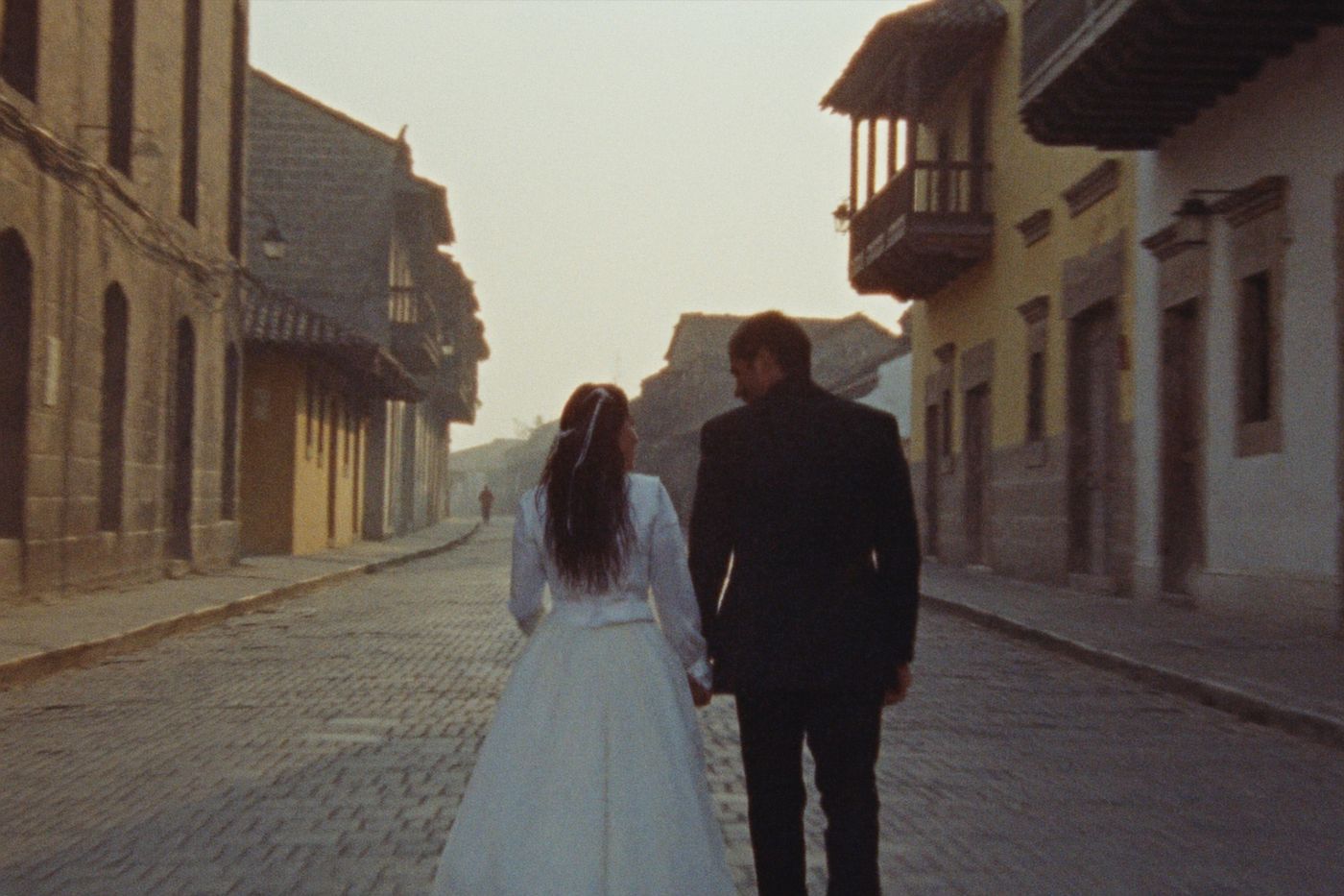 A couple walking a colonial street at dawn, balconies and shuttered windows above them