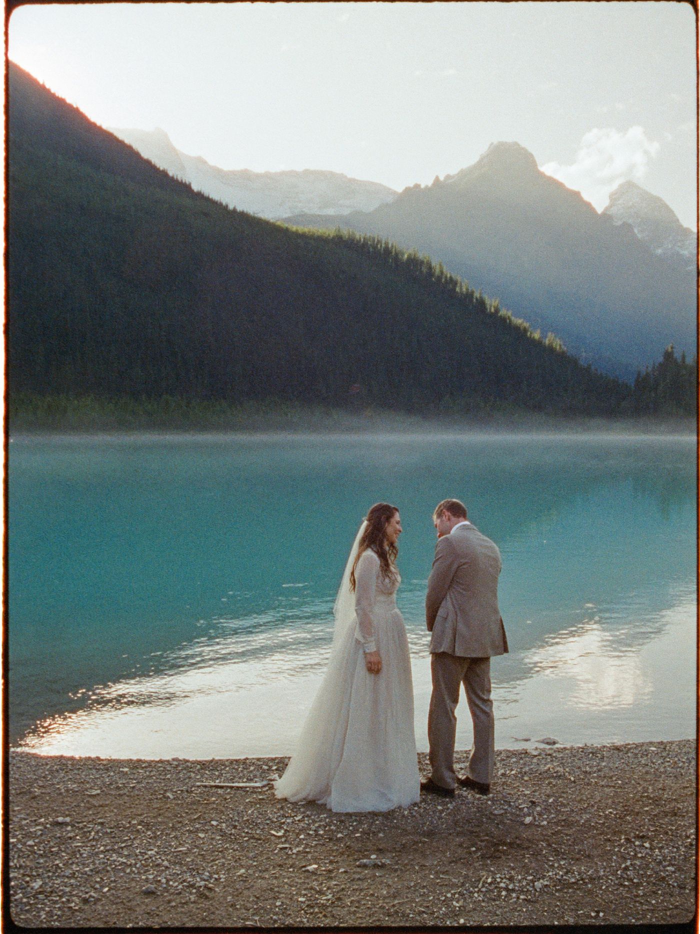 A couple on the shore of a turquoise glacial lake in the Canadian Rockies at dawn