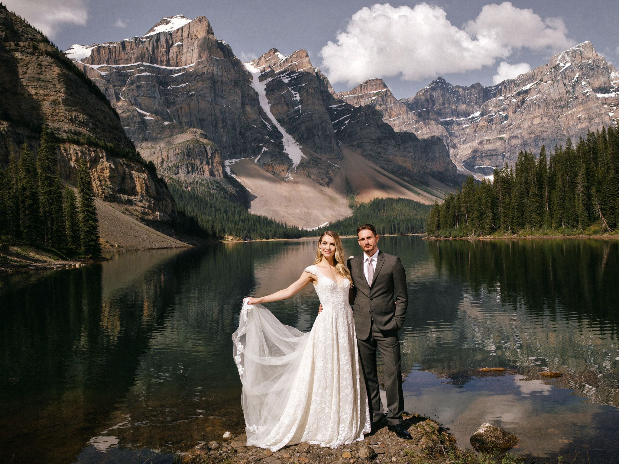 A couple on the shore of a turquoise mountain lake in Banff at first light