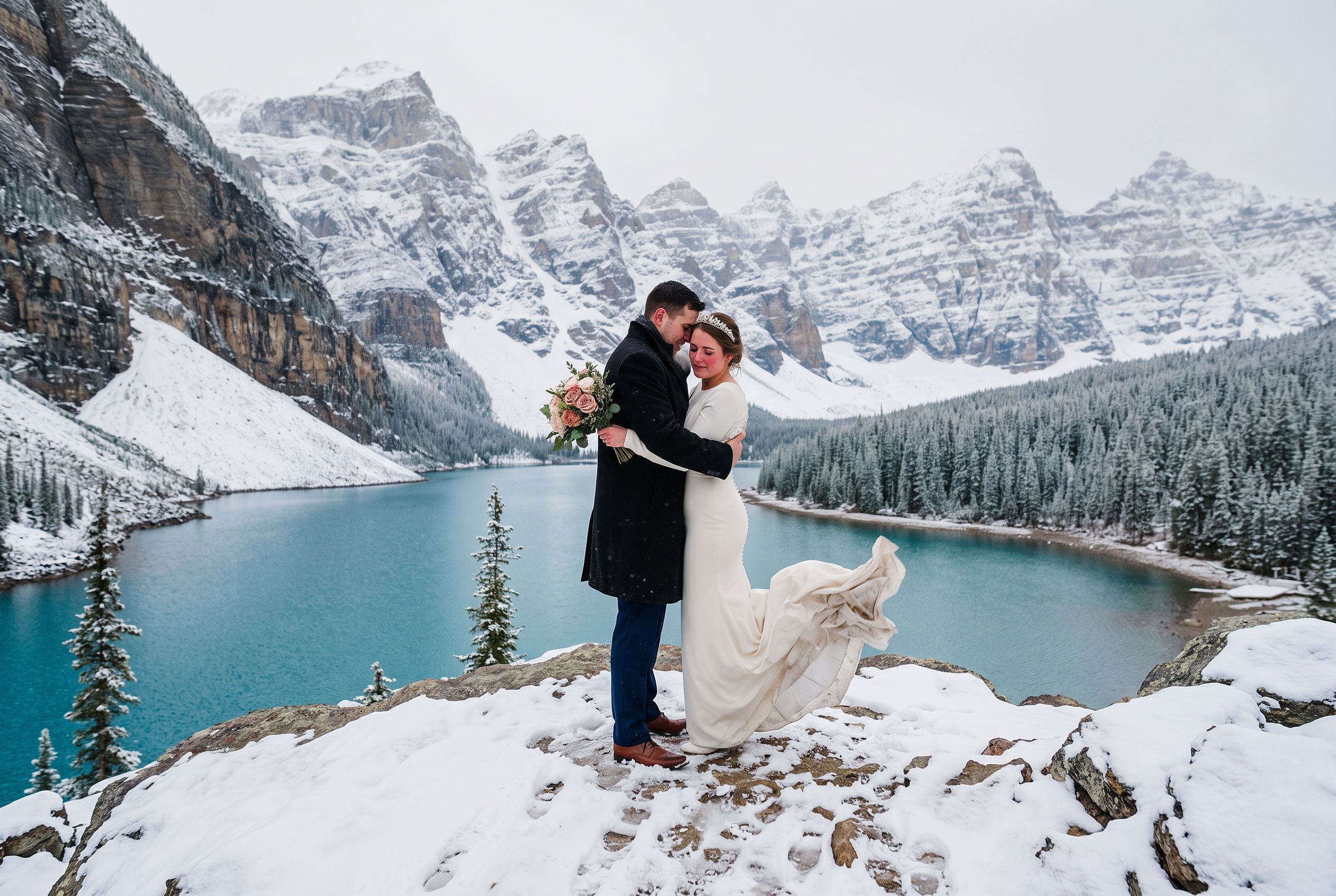 Snow on the shore of a turquoise glacial lake in Banff with jagged peaks behind