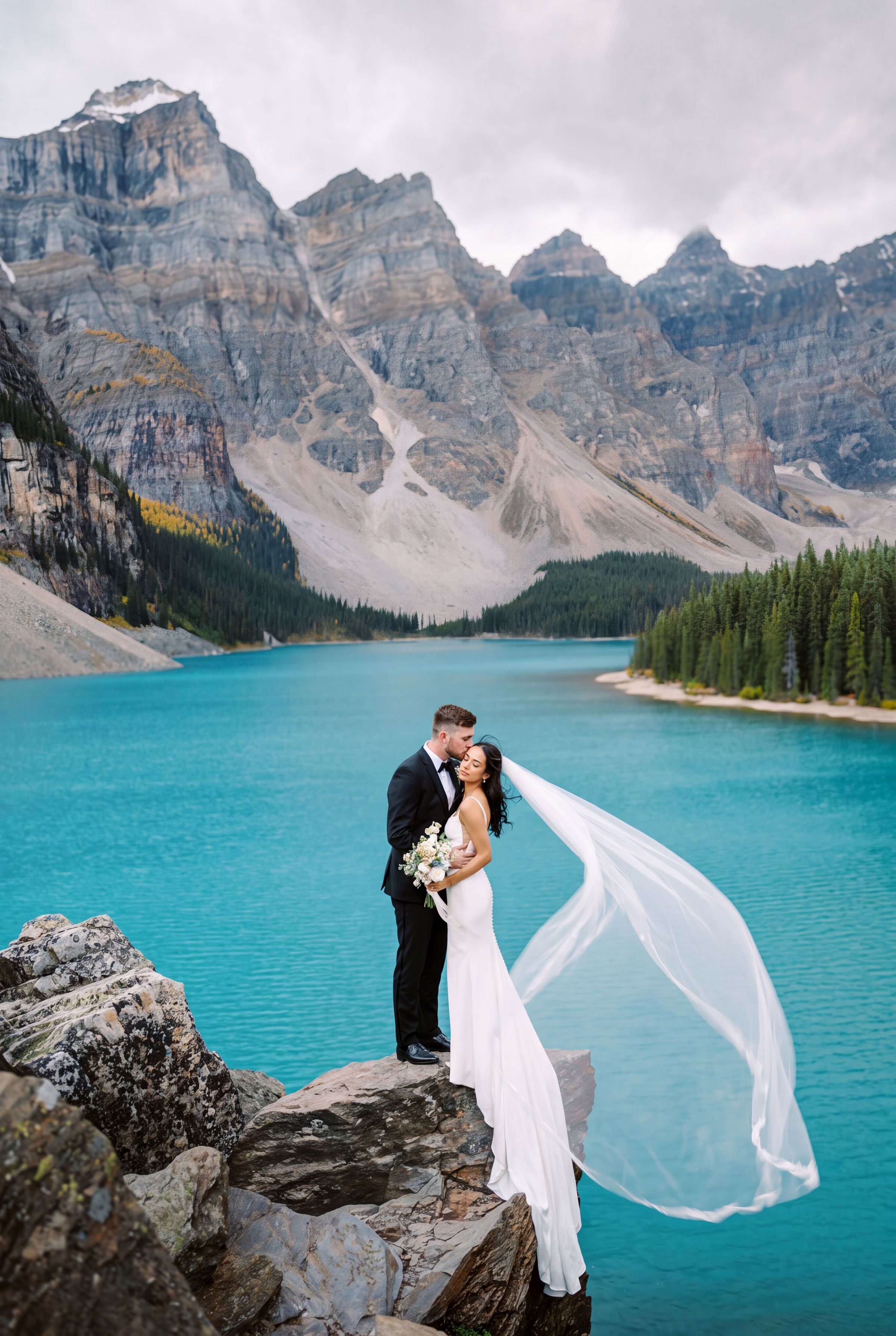 A couple with a veil lifting in the wind beside Moraine Lake