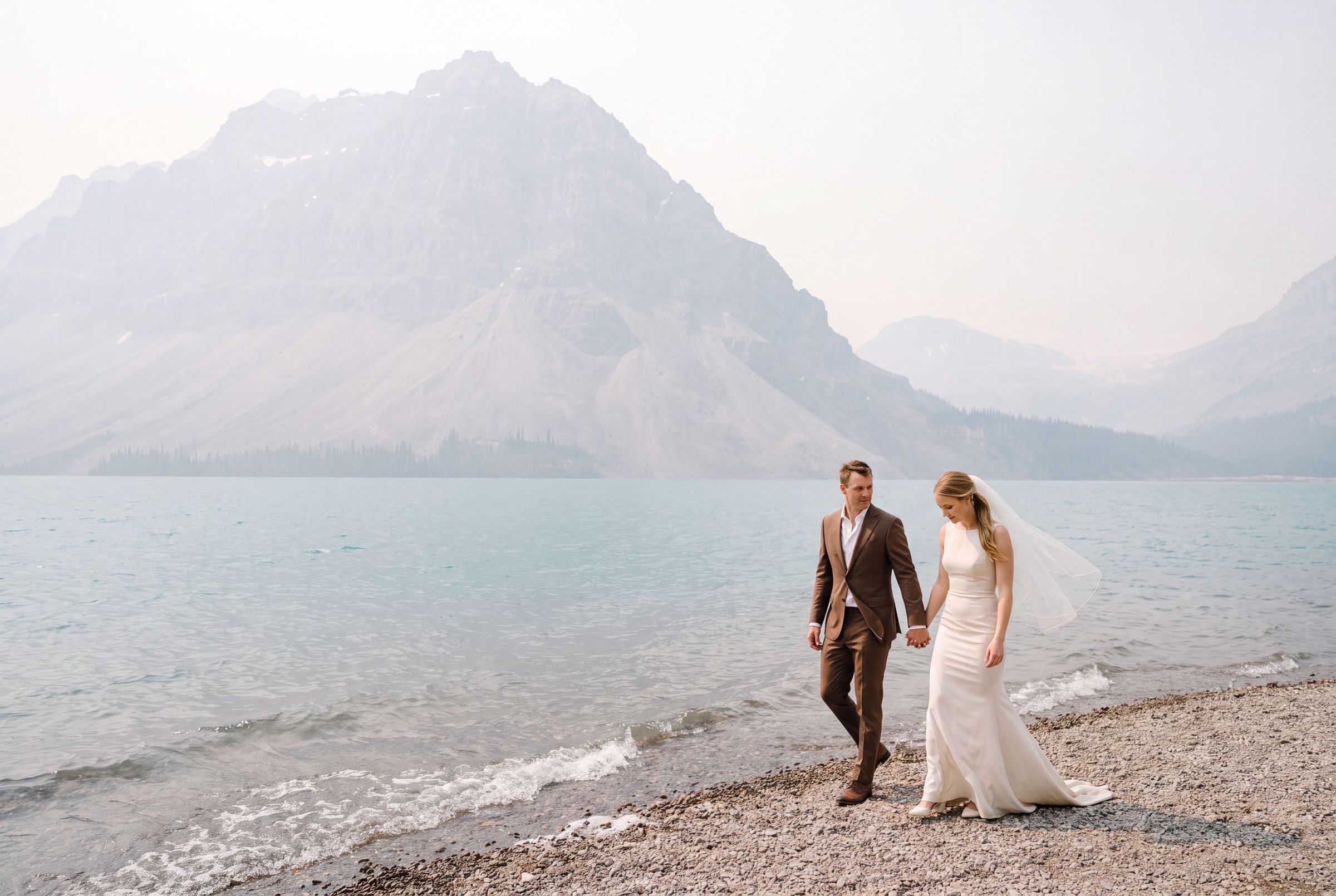 A couple walking the shore of a mountain lake under mist