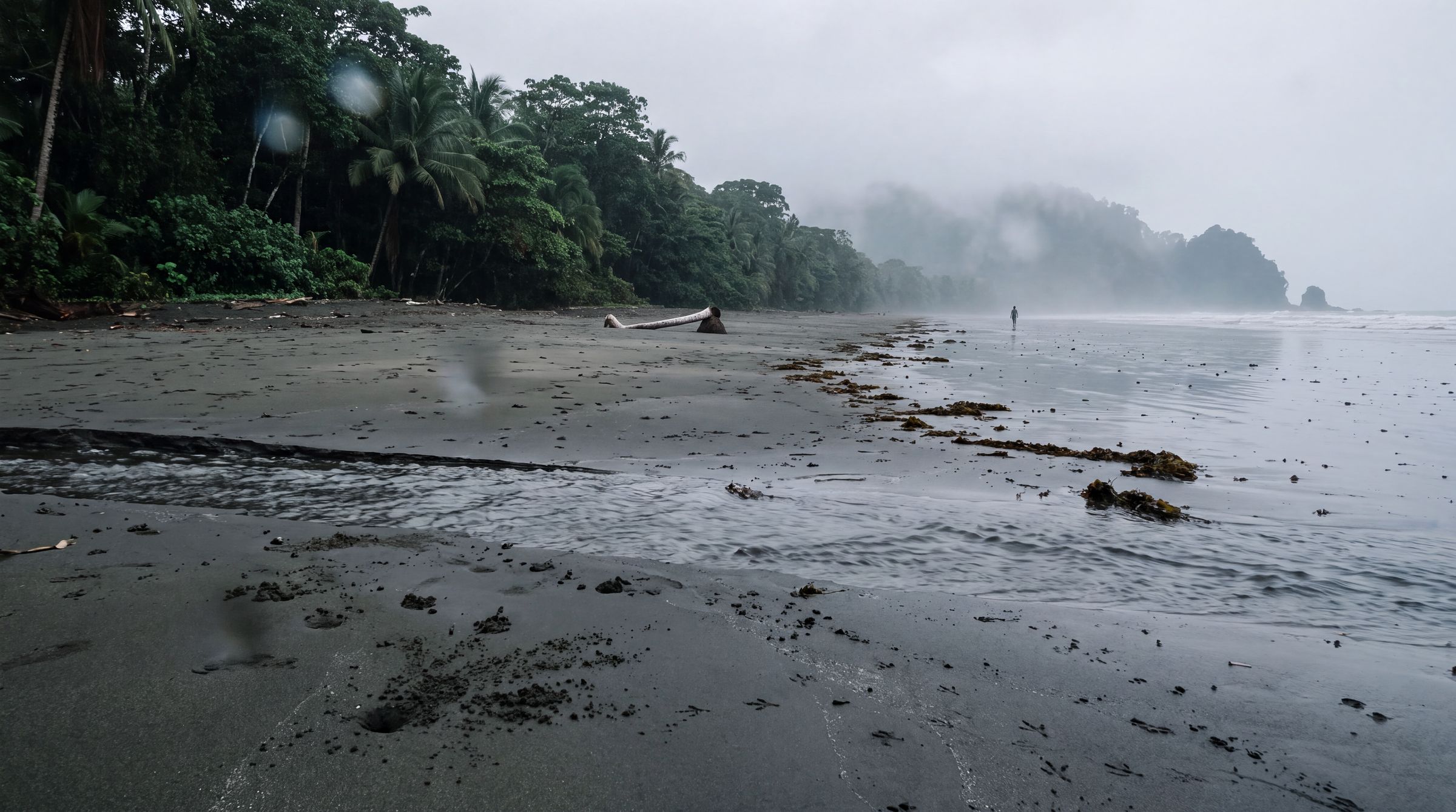 Rain streaking the lens above a dark sand beach and grey ocean in Chocó