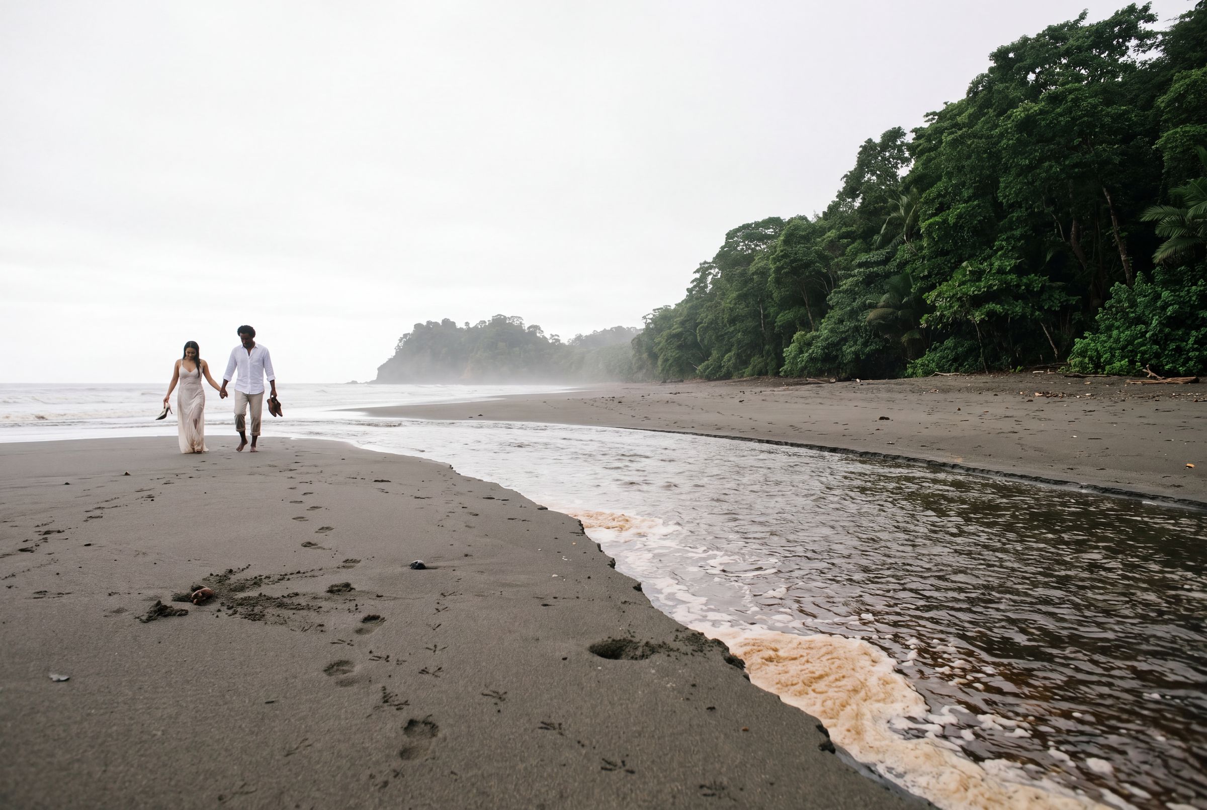 A wide dark beach at low tide in Chocó with jungle behind and cloud over the water