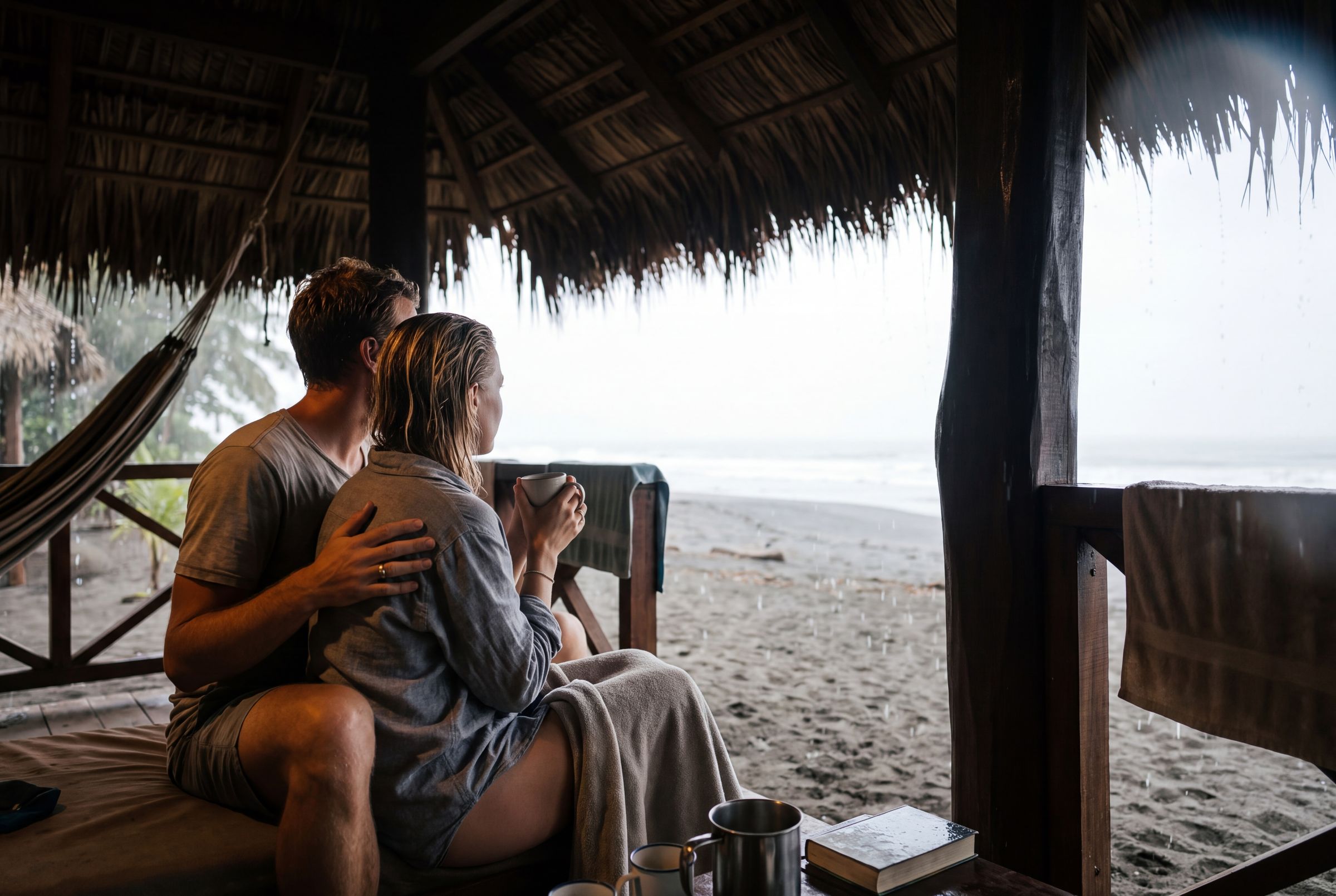 A couple on a dark beach pointing out to the grey Pacific with jungle headlands behind