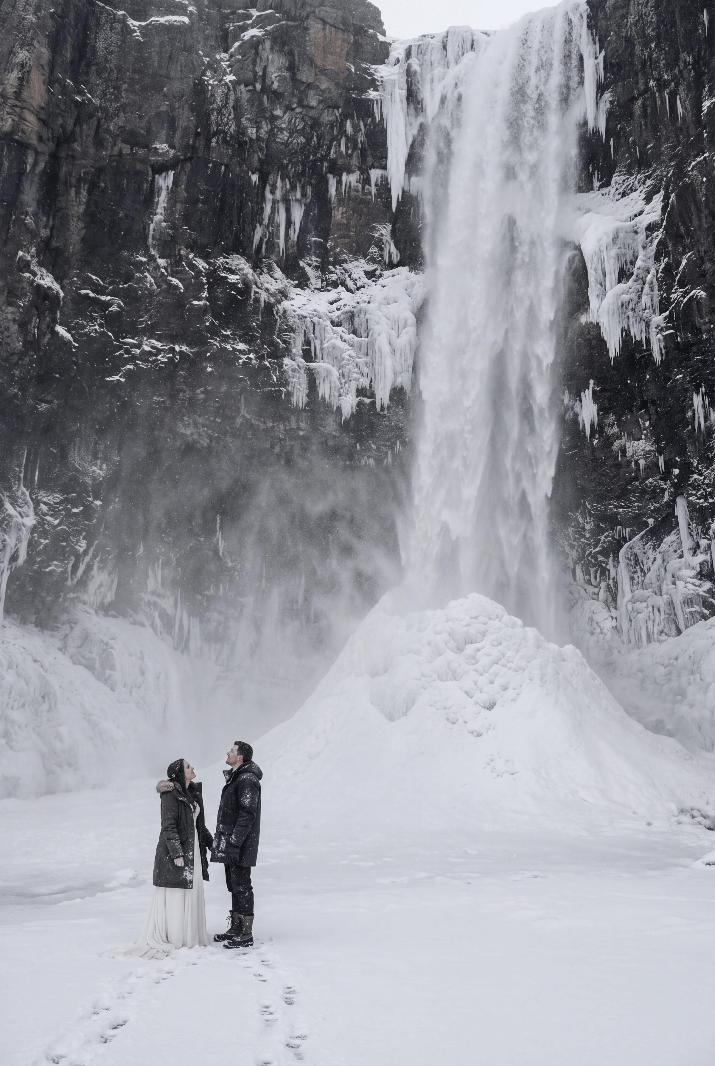 Two people alone at the foot of a frozen waterfall in Québec