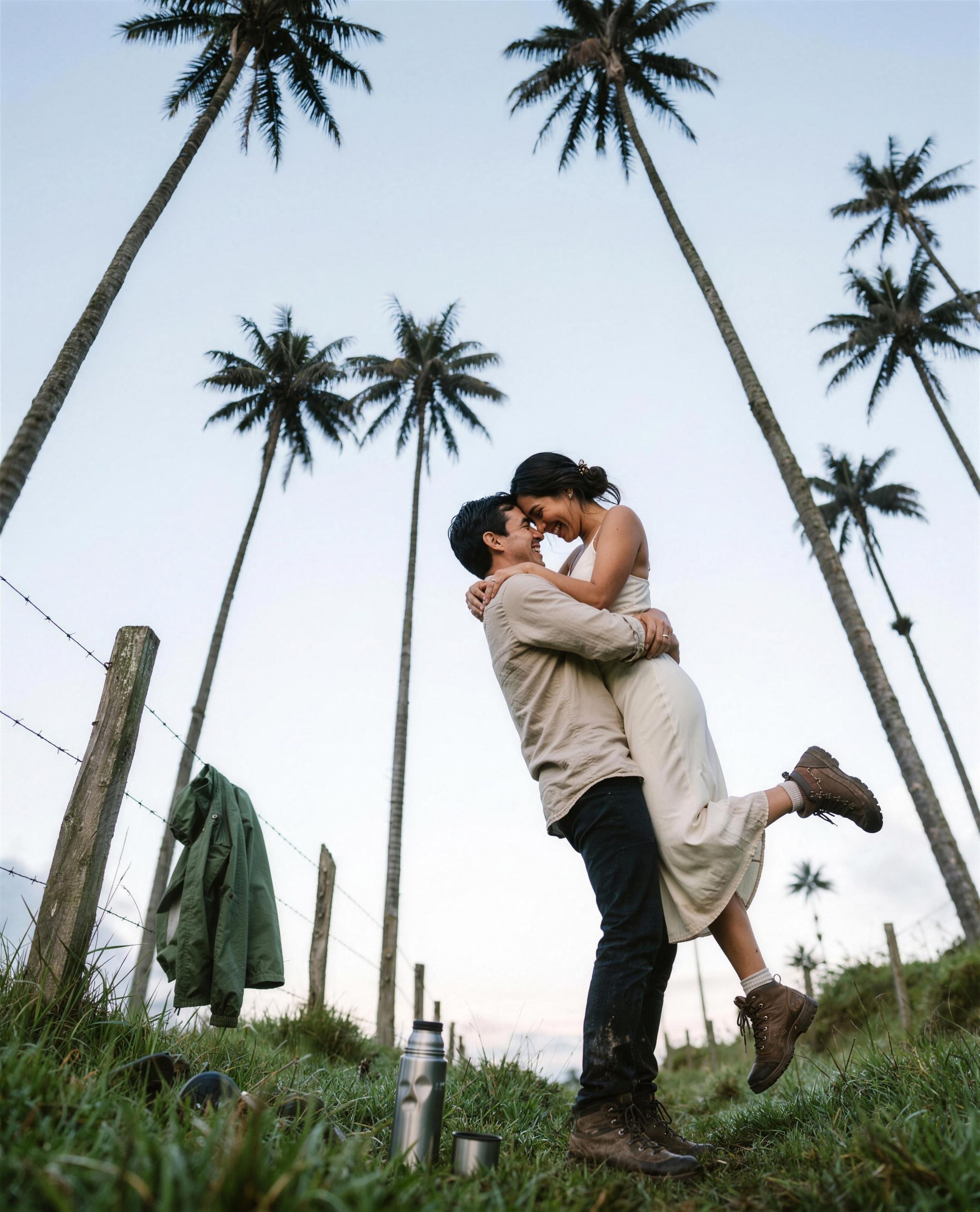 Groom lifting his bride off her feet on the floor of the Cocora Valley at first light, sixty-metre Quindío wax palms towering above them and a thermos left in the wet pasture grass