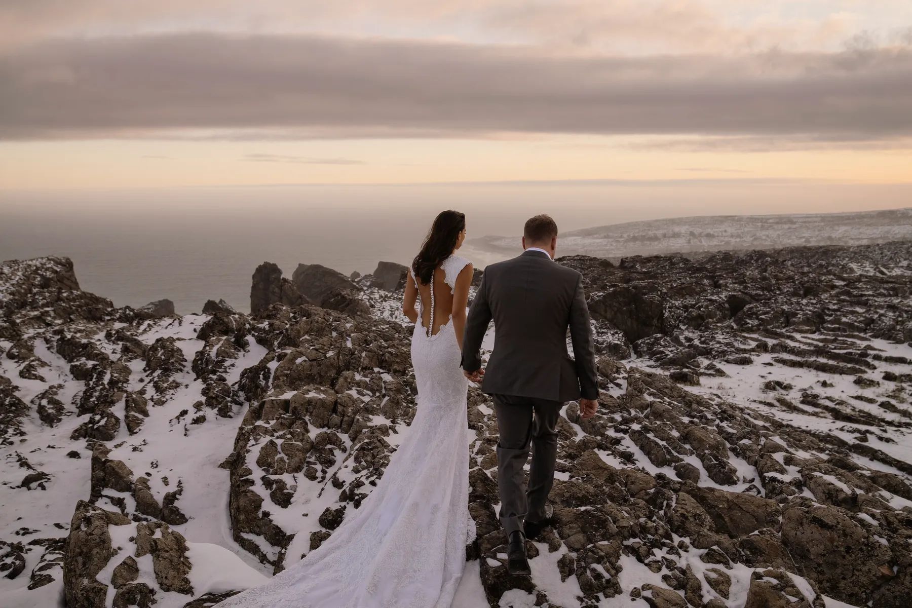 Couple walking a snowy rocky shoreline at sunset