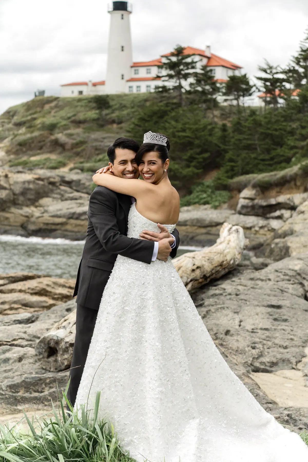 Couple embracing on driftwood at Lighthouse Park with the lighthouse above them