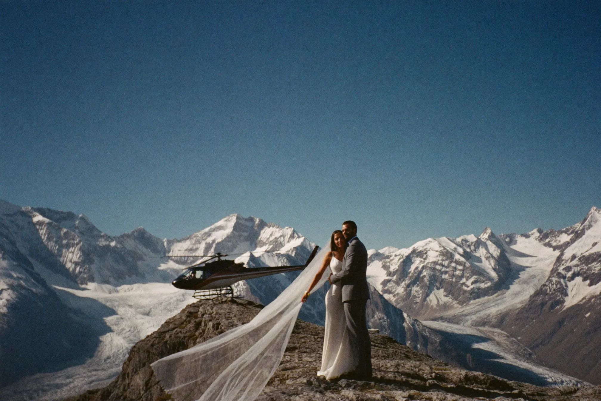 A couple walking toward a helicopter on a remote alpine ridge in the Canadian Rockies
