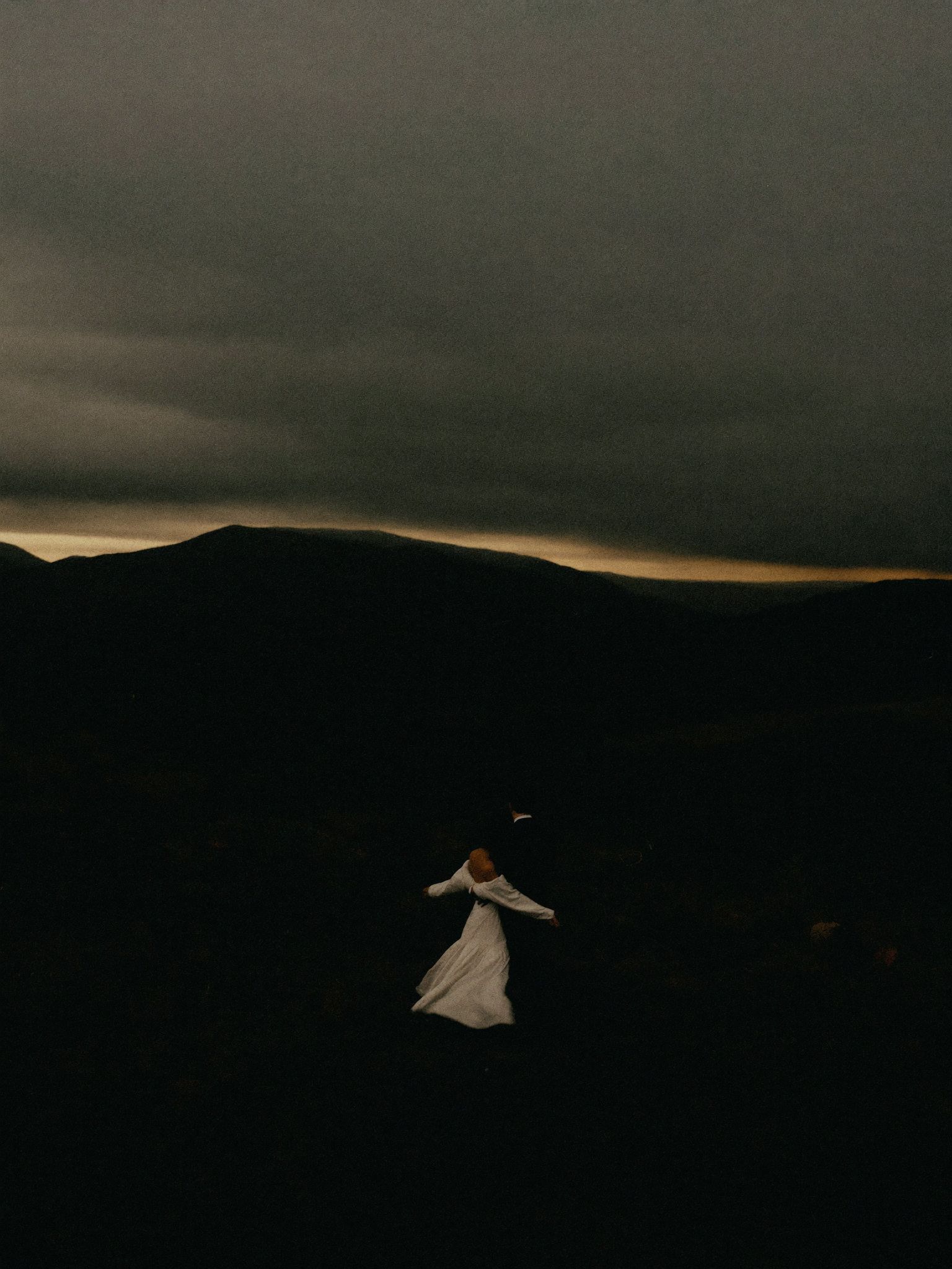 A bride alone against a vast, moody landscape at dusk