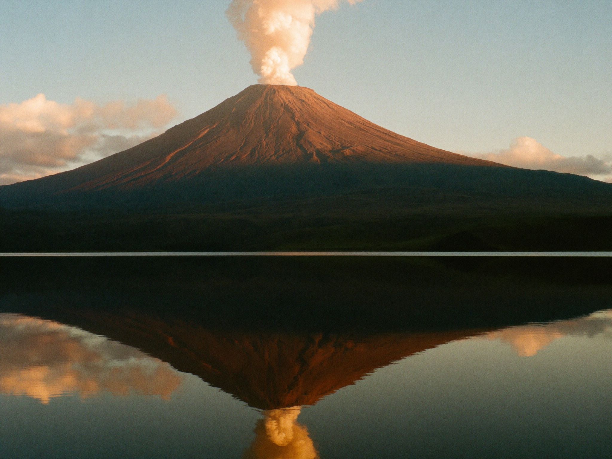 Arenal volcano reflected in still water at dawn with forest along the shoreline