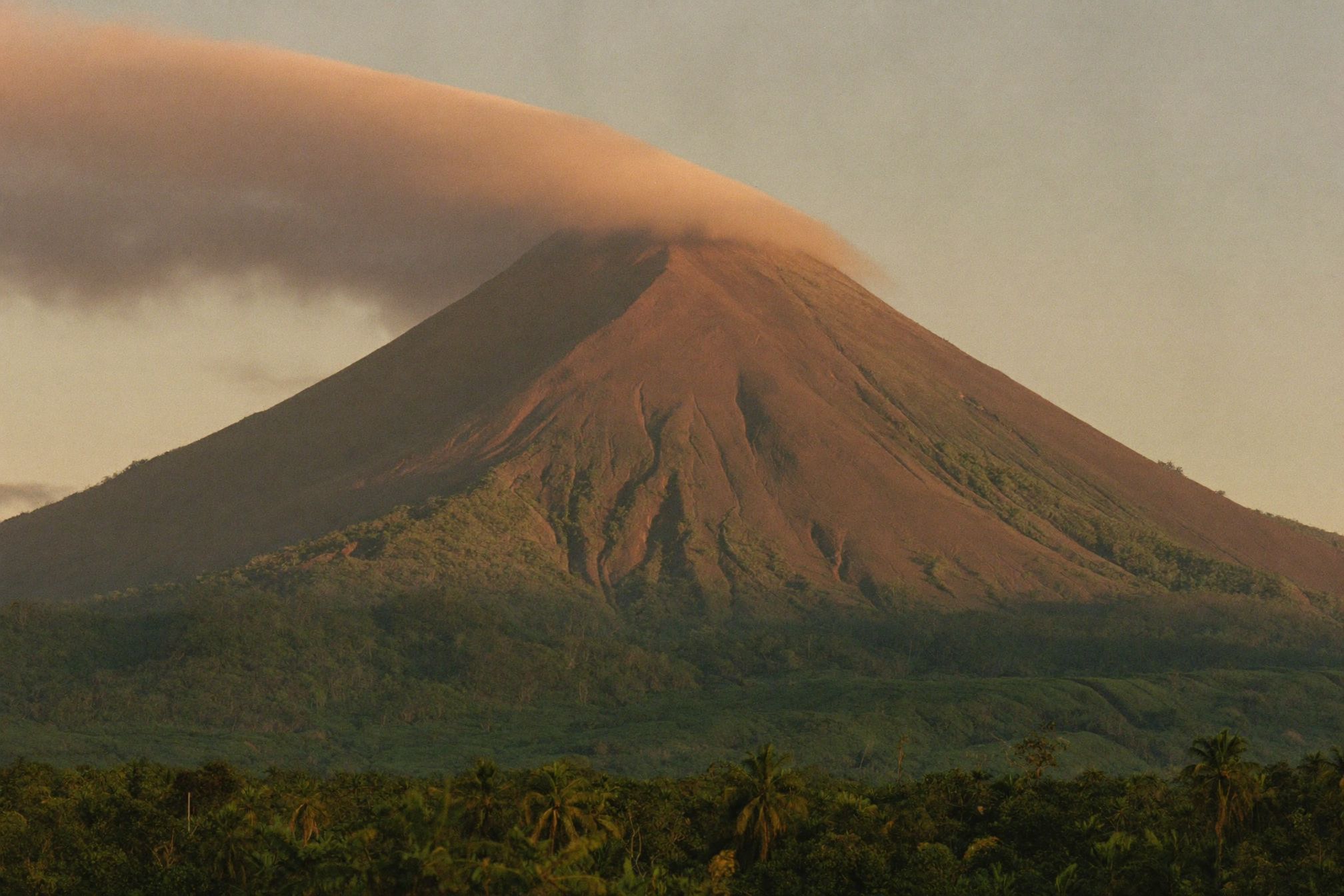 The cone of Arenal volcano standing over unbroken rainforest at last light