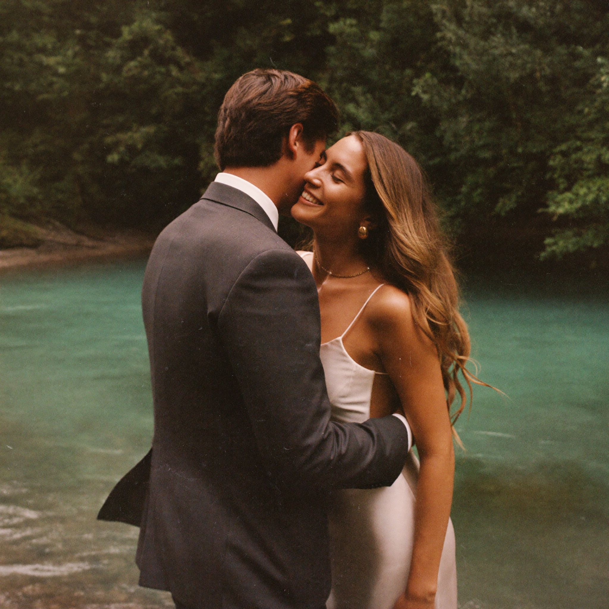 A couple standing at the edge of a calm turquoise cove in the rainforest