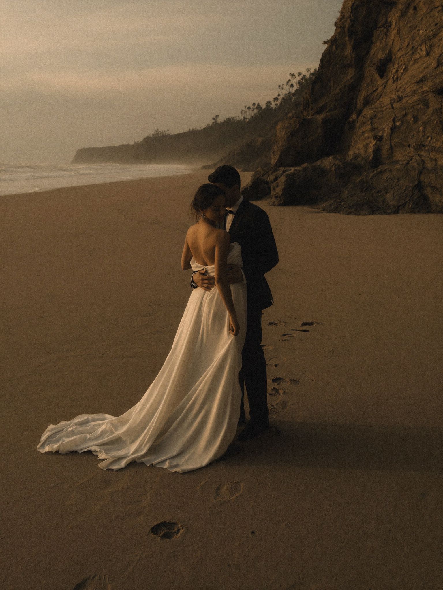 A couple standing under a headland on an empty beach