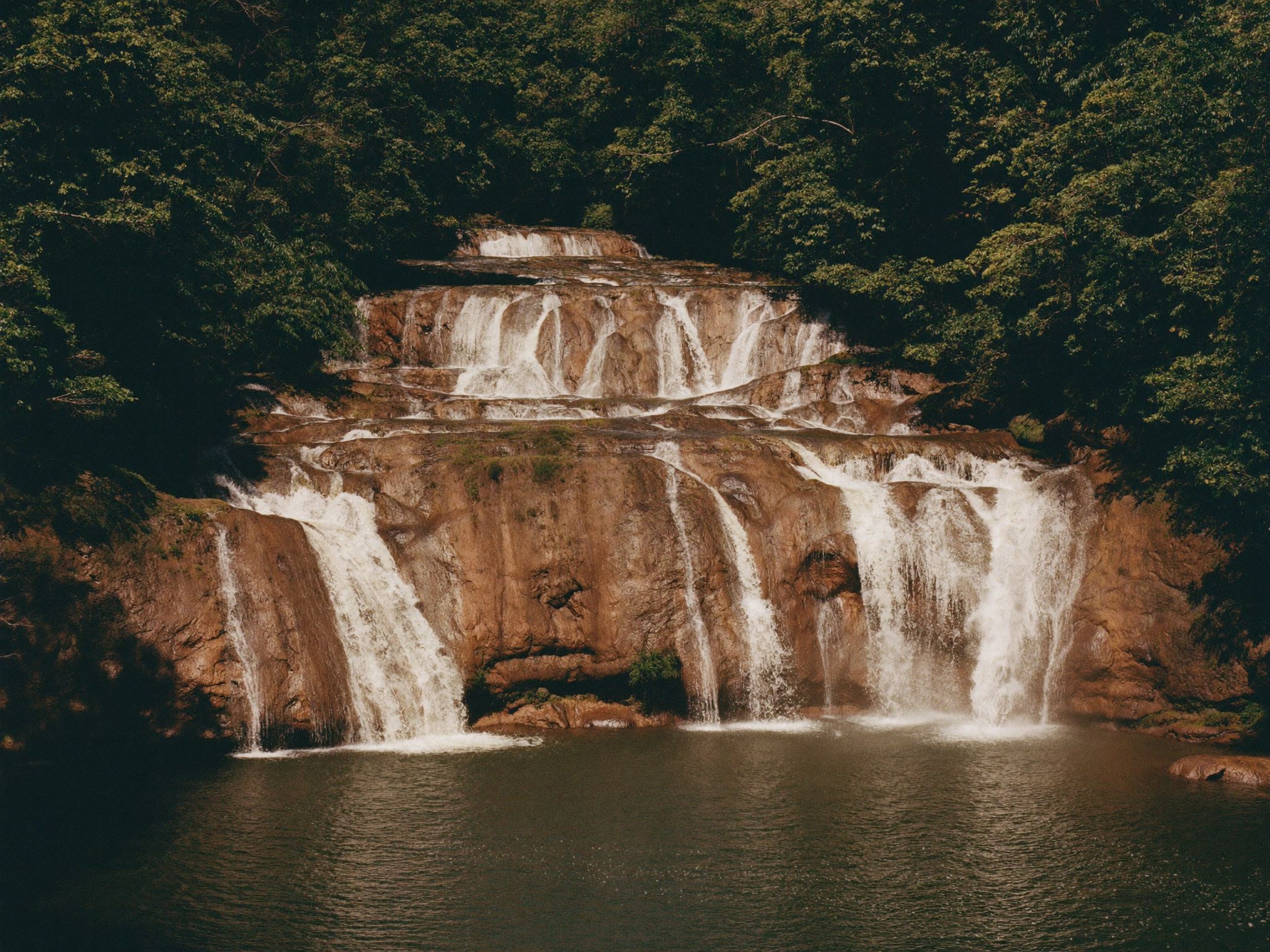 Tiered waterfalls dropping into a green pool in the rainforest