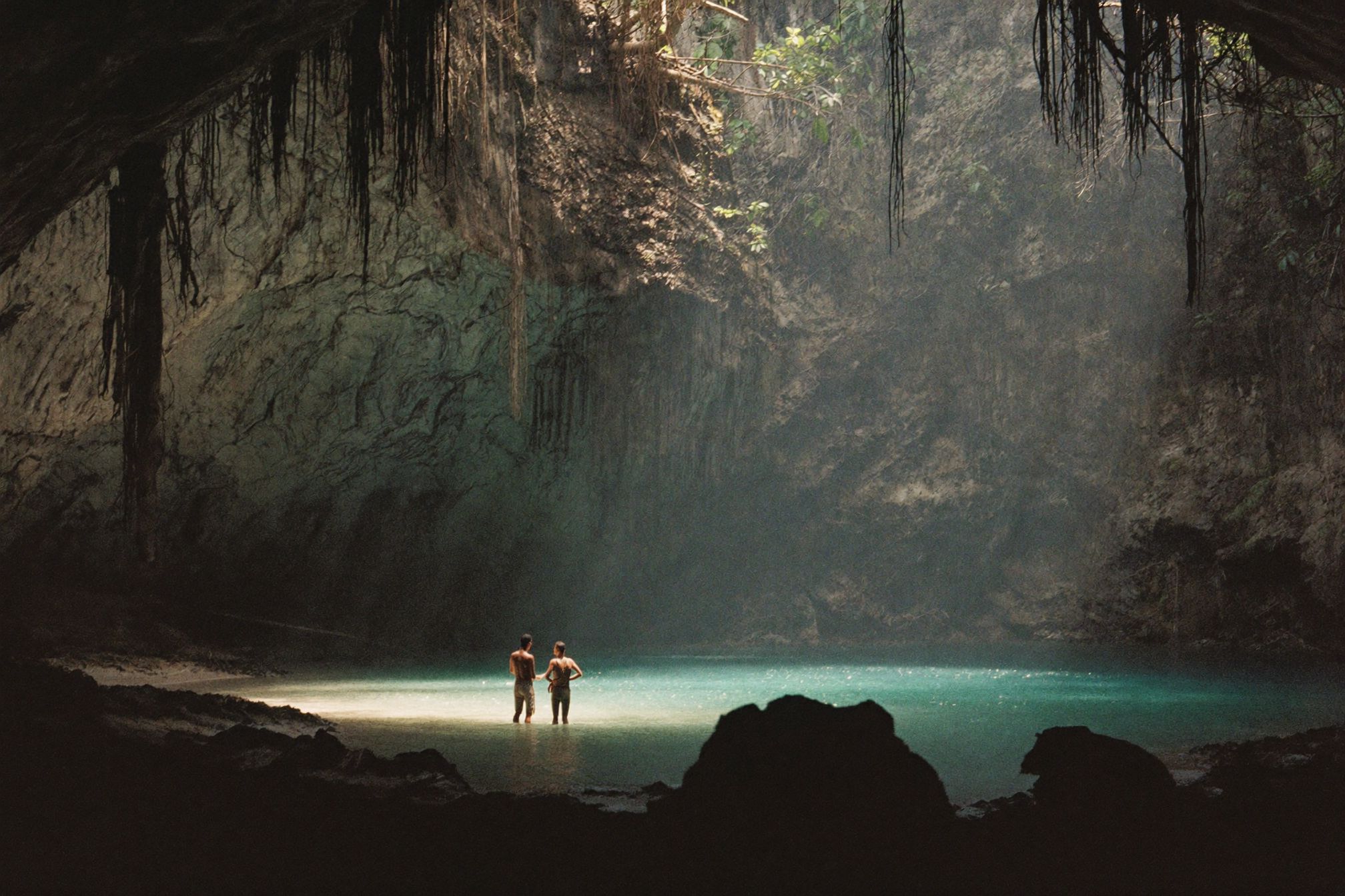 A wide cenote with light falling through the opening onto still freshwater